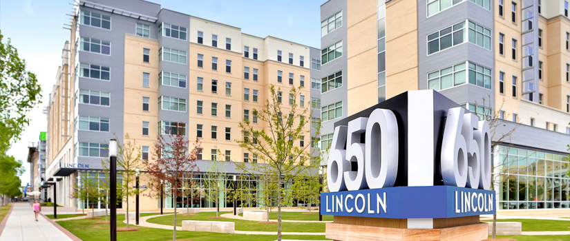 A sign for 650 Lincoln sits in the foreground, with small trees and green space in front of an apartment building with multiple stories.