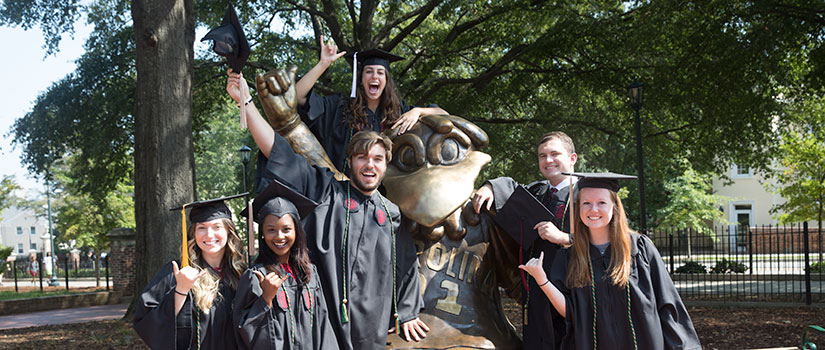 Image of students celebrating in graduation cap and gown in front of Cocky statue