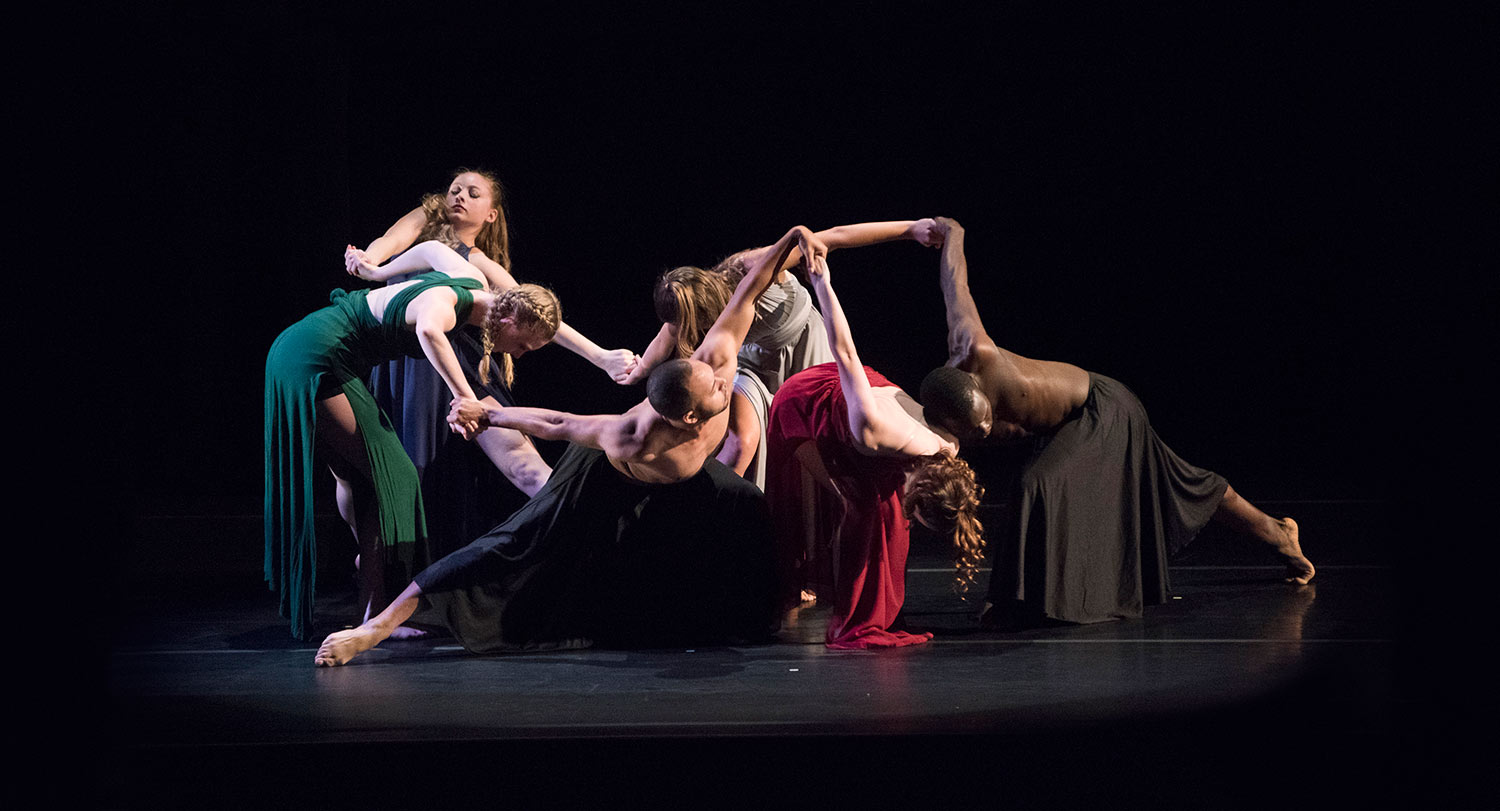 Group of students dancing in full costume on a dark stage. 