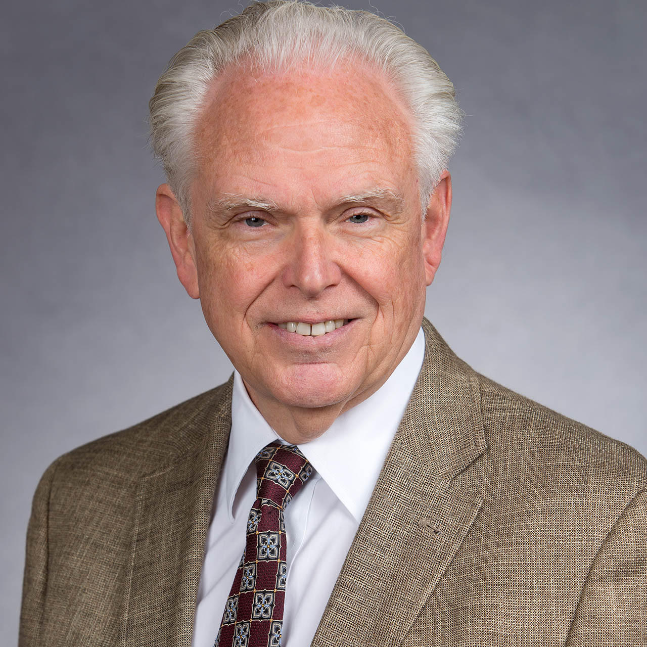 Dr. Bill Mobley, a white man with light colored hair in a tan suit, smiles at the camera.