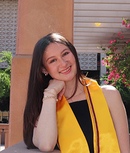 woman with dark hair and yellow sash on smiling