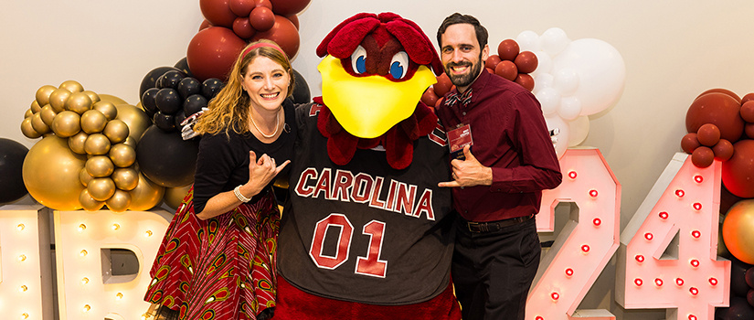 Two people pose with Cocky at the HRSM Homecoming Party