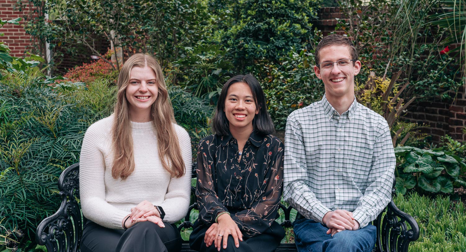 three people sit on a bench in a garden setting