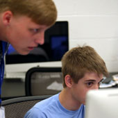 one student helps another at a computer