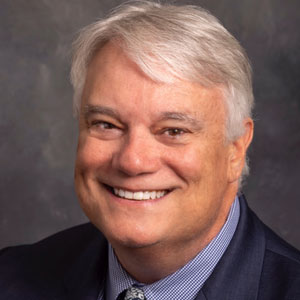 man with white hair in a blue suit, smiling