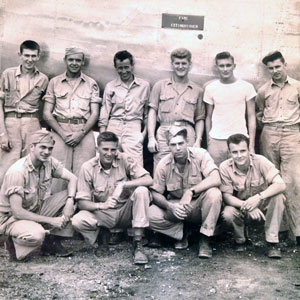 Ten soldiers pose beside a plane in a World War II archive photo.