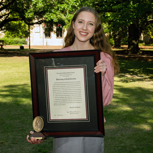 Charlotte pollack stands on the horseshoe holding a large framed award