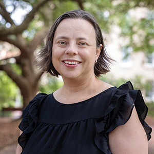 April Hiscox smiles in front of a tree.