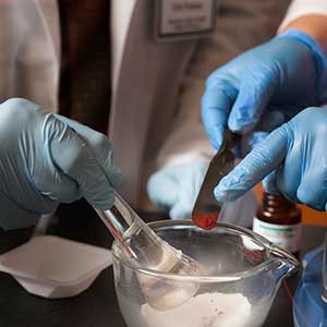 Two sets of hands work to compound medicine in a pharmacy.