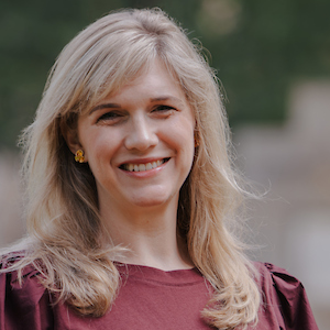 Blond-haird woman in garnet shirt smiles while standing in front of gray monument