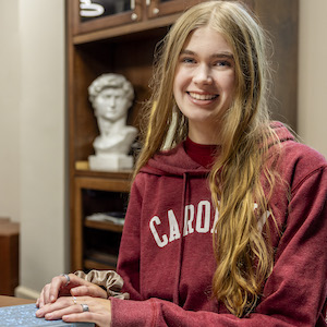 Maleah Anderson sits at a desk with a bookcase on the background