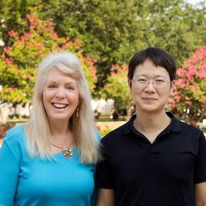 Susan Richardson stands outdoors smiling next to Jiafu Li on the USC campus with greenery and flowers blooming in the background.