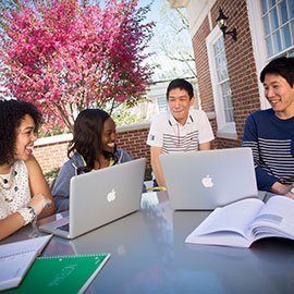 Four students sit at a table on the SJMC patio with laptops