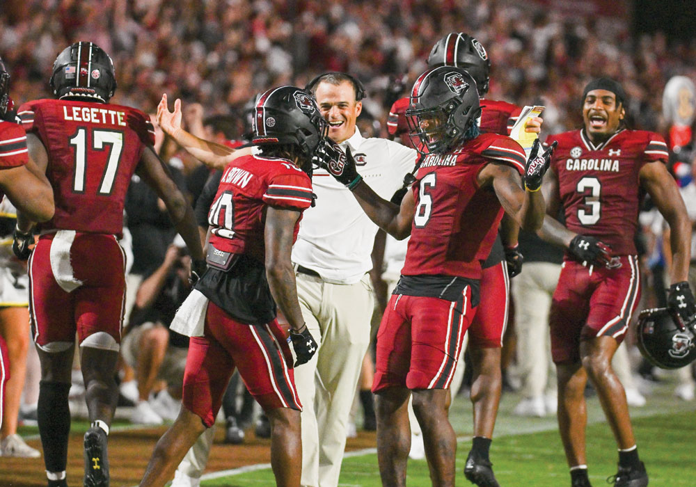 Shane Beamer celebrates on field with players after a successful play.