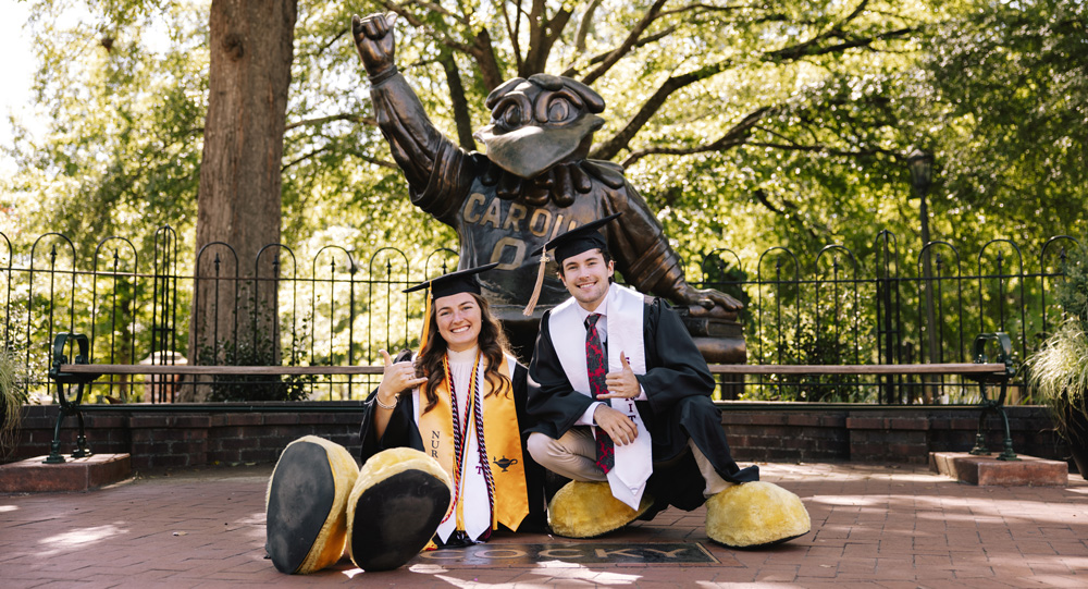 John and Nicole pose with their Cocky feet on in front of the Cocky statue.